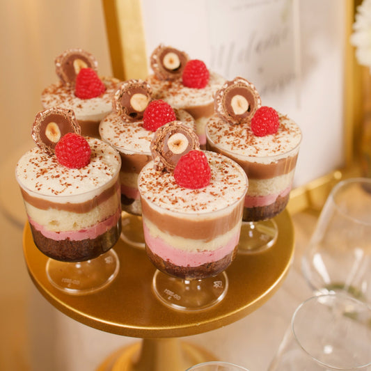 Small dessert cups with red berries and chocolate elements on a gold stand.
