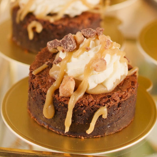 Chocolate dessert with whipped cream and caramel drizzle on a gold plate.